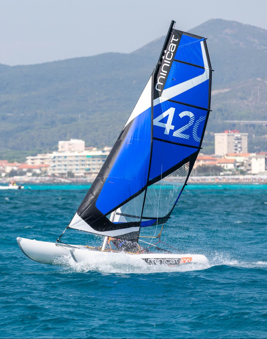 Sailboat MiniCat with a blue and black sail on the water with mountains in the background