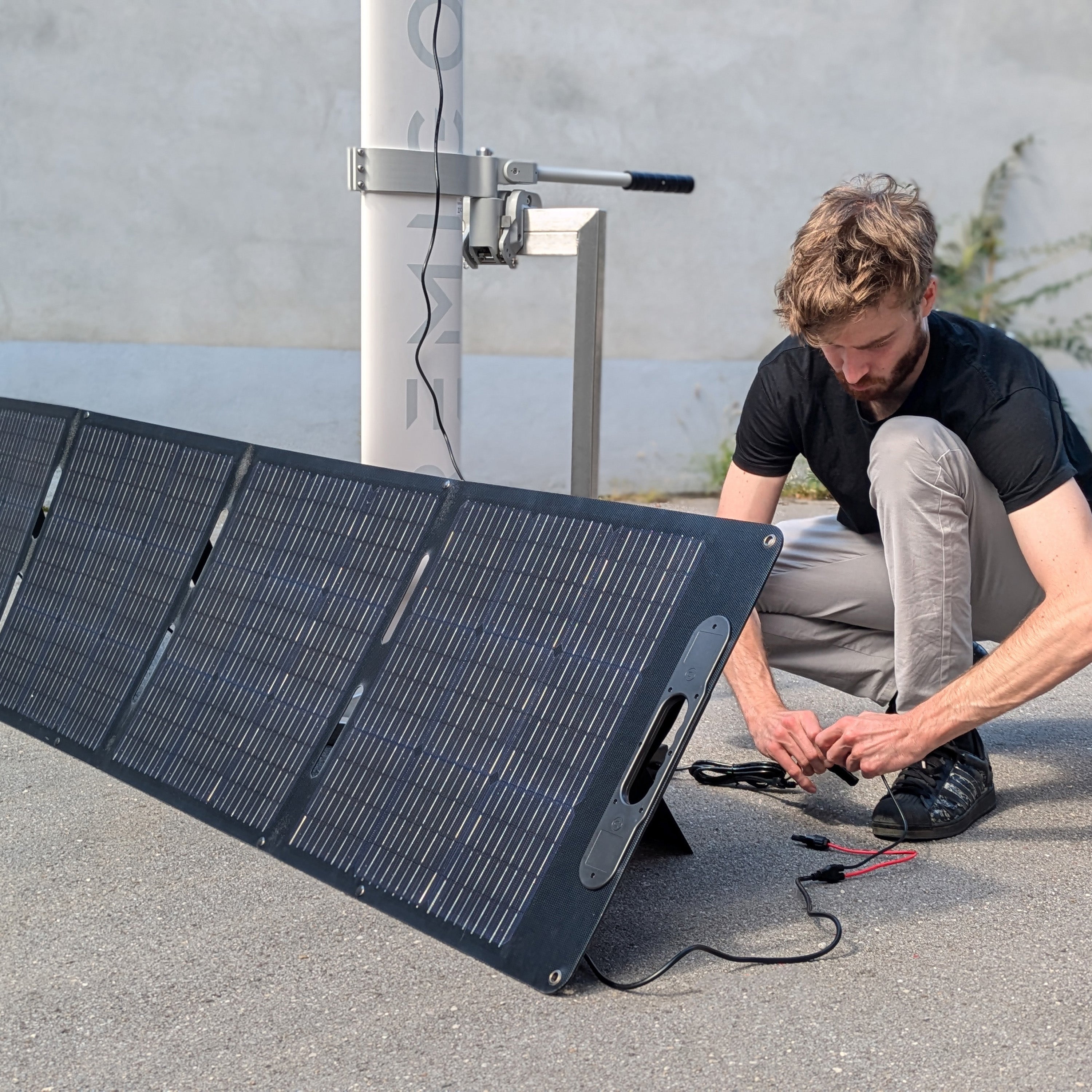 Person setting up a solar panel on the ground with a concrete wall in the background